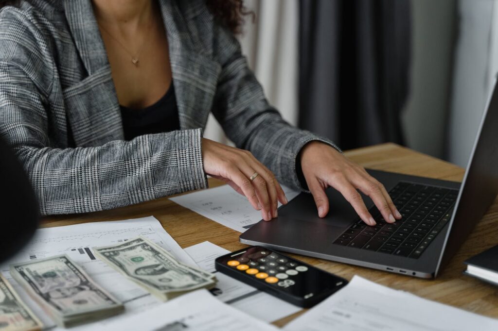 Women typic on laptop with money beside her.